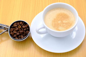 Coffee cup and beans on wooden kitchen table. Top view with morning sunlight