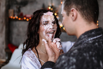 The guy tries to give the girl a finger smeared in cake to lick. The action takes place in the kitchen, decorated for the celebration of Christmas and New year