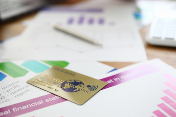 Close-up of golden plastic credit card on business papers. Annual report with charts and diagrams. Online shopping and payment. Financial investment and economy concept