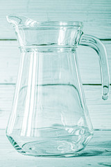 An empty glass carafe for water stands on a white wooden background