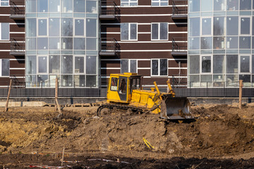 The bulldozer moves and spreads the soil and rubble on the embankment of the road. Work in progress on a new apartment block.  Construction Site of New Building