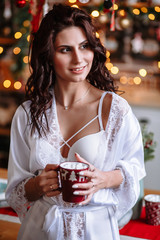 A girl in a dressing gown holds a Cup of cocoa. The action takes place in the kitchen, decorated with a Christmas tree