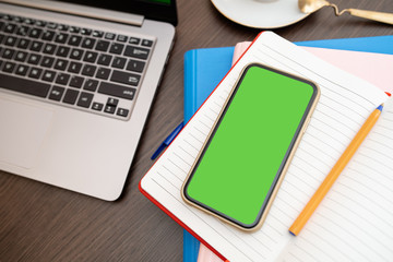 Cropped shot top view of smartphone mockup at the wooden office desk. Blank screen mobile phone for graphic display montage.