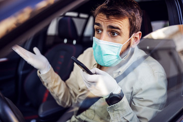 Man with protective mask and gloves driving a car talking on mobile phone smartphone. Infection prevention and control of epidemic. World pandemic. Stay safe.