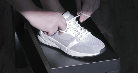 Human hands lace up gray sneakers 
