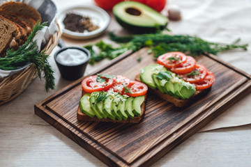 Fototapeta na wymiar Healthy vegan homemade sandwich, avocado and tomatoes with dark grain bread on a wooden board.