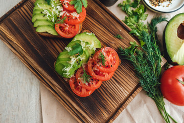 Healthy vegan homemade sandwich, avocado and tomatoes with dark grain bread on a wooden board.
