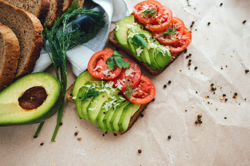 Healthy vegan homemade sandwich, avocado and tomatoes with dark grain bread on a craft paper background.