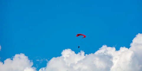 Alone paraglider flying in the blue sky against the background of clouds. Paragliding in the sky on a sunny day.