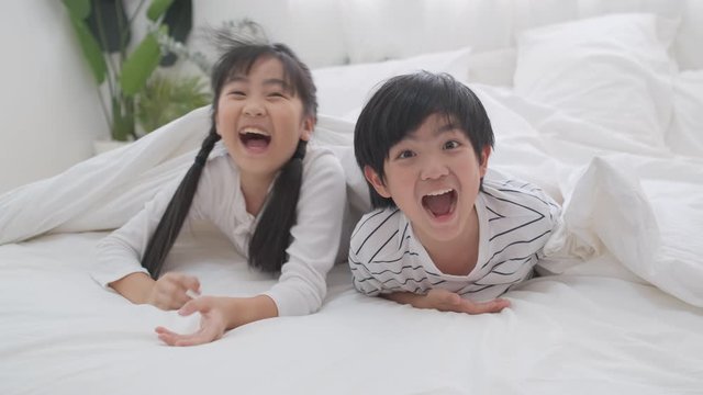 Two sister and brother plan fun with blanket on bed and they look happy.
