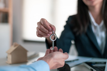 Young Asian man receiving new apartment or room key from realtor or real estate sales agent after finish a rental or buying contract.