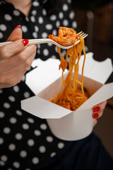 Girl eats pasta with shrimp from a white box with a fork. Close-up