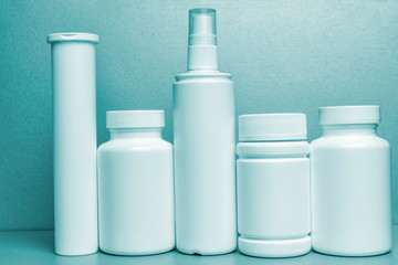 5 white vials without labels for medicines, vitamins, sprays, liquids are on a gray shelf. mockup for pharmacy and store design. blue tinting