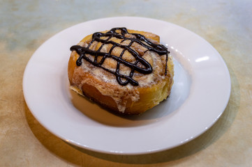 Cinnabon. Cinnamon roll decorated with chocolate on a white plate on blue and yellow kitchen table background