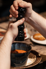 hands hold pepper shaker and add spices to soup. Close-up.