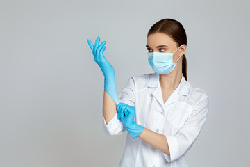 woman doctor in white uniform wearing mask and rubber gloves on gray background. copy space
