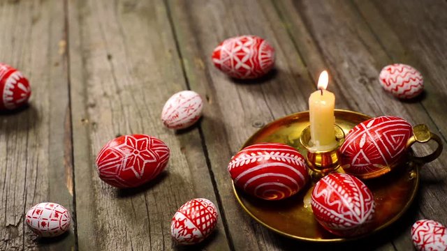 Red easter eggs with folk Ukrainian pattern lay around and on candlestick with burning candle on vintage boards background. Ukrainian traditional eggs pisanka and krashanka