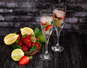 Cooling summer strawberry mojito cocktail with lemon and mint on a dark background. Fresh strawberries and piles of ice on a table with two glasses of drink.