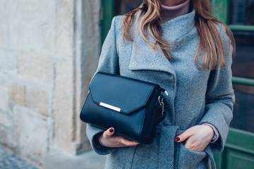 Female purse. Fashionable spring accessories. Stylish woman wearing grey coat and holding black handbag outdoors. - obrazy, fototapety, plakaty
