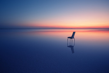 Chair among smooth water of lake at sunset
