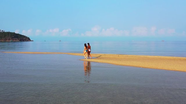 Young women walking on sandy stripe washed by calm clear water of shallow lagoon on beautiful bay of tropical island in Vietnam