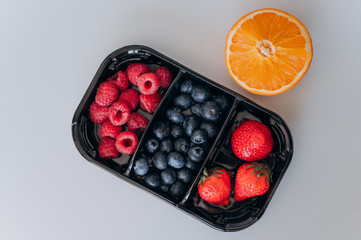 juicy fresh blueberries, raspberries and strawberries lay in a black tray next to an orange
