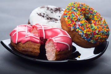 donuts with icing and chocolate in a plate on a dark background