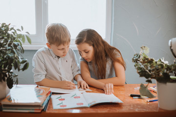 The boy and girl reading book at home during CoVid-19 quarantine, distance learning online with a laptop, a child doing homework for school. Children stayed at home.