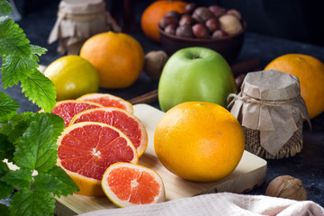 Sliced grapefruit is on a wooden chopping Board. On the table are nuts, herbs, apples and lemons, honey in a jar