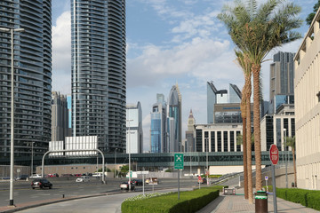 Fototapeta na wymiar Road with cars near the skyscrappers in Dubai. Green palm near the road.