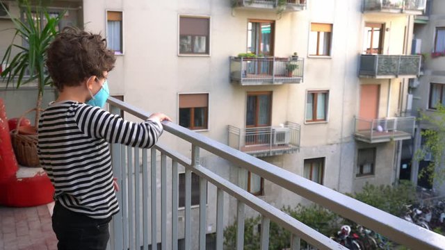 Europe, Italy , Milan - children boy  five years old with mask at home during quarantine due n-cov19 Coronavirus outbreak epidemic  - 
lifestyle and  play throwing paper airplanes from the balcony