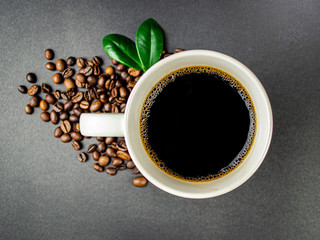 Cup of coffee with roasted beans and green leaves on black background