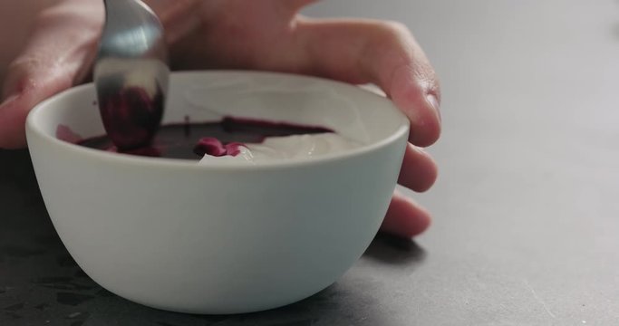 Slow motion man hand mix bilberry juice with white yogurt in white bowl on concrete surface