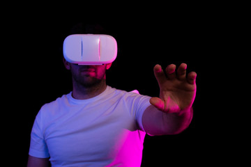 Chico con unas gafas de realidad virtual sobre un fondo negro y colores. Un brazo estirado hacia...