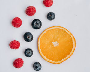 juicy fresh berries blueberries and raspberries lie on a white table next to a slice of orange