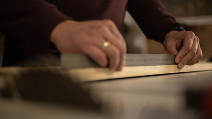 The carpenter measures the wooden board and marks it with a graphite pencil. Meter in the background