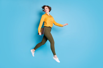 Full body profile photo of beautiful business lady jumping high up hold notebook going conference wear yellow shirt green pants shoes isolated bright blue color background