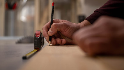The carpenter measures the wooden board and marks it with a graphite pencil. Meter in the background