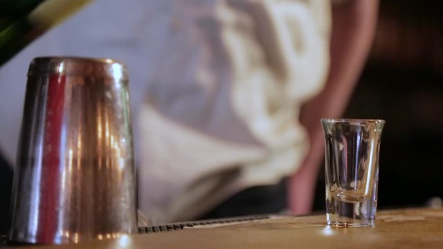 A bartender placing a shot glass on a bar and pouring a shot of whiskey