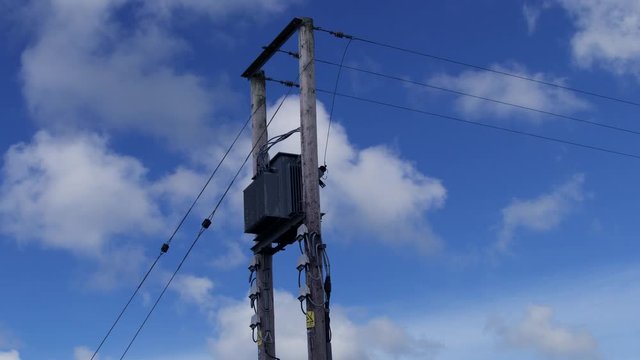 Timelapse of fast moving clouds in a blue sky passing wooden electricity pylons and cables. England, UK.