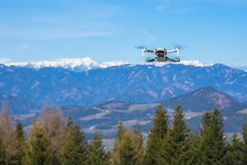Fototapeta na wymiar White drone with photo camera flying in the blue sky and beautiful mountain landscape in the background