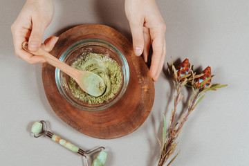 Close up of woman's hands in white shirt mixing organic ubtan with a spoon in wooden bowl. Traditional natural herbal cosmetic agent for skin and hair care handmade creation.