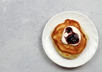Pancake with sour cream and jam on a round plate on a light gray background. Top view, flat lay .