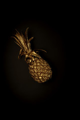Golden pineapple on a black background, stylish minimalistic composition with copyspace for ad. Fashionable trendy combination of colors. Food, fruits, sweets, summer vibes concept. Poster, wallpaper.