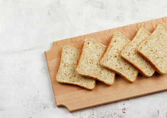 Slices of multigrain bread on a wooden cutting board on a light gray background. Top view, flat lay