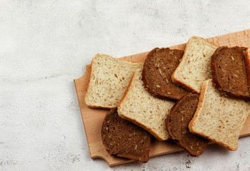 Slices of multigrain bread and rye bread on a wooden cutting board on a light gray background. Top view, flat lay