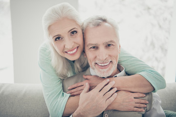 Close up photo of cute lovely grandparents hugging looking wearing teal brown sweaters in apartment...