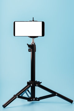 Mobile phone mounted on a tripod with a white display free for images and text, blue isolated background.
