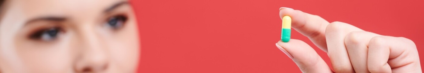 Female doctor holds colored tablet. Nurse shows a capsule with medicine. Isolated red background