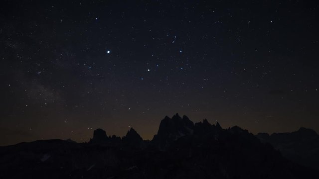 Time lapse of milky way and night sky with stars over Dolomite Alps at Three Peaks in summer, clouds coming in, mountain silhouettes, South Tyrol Italy
